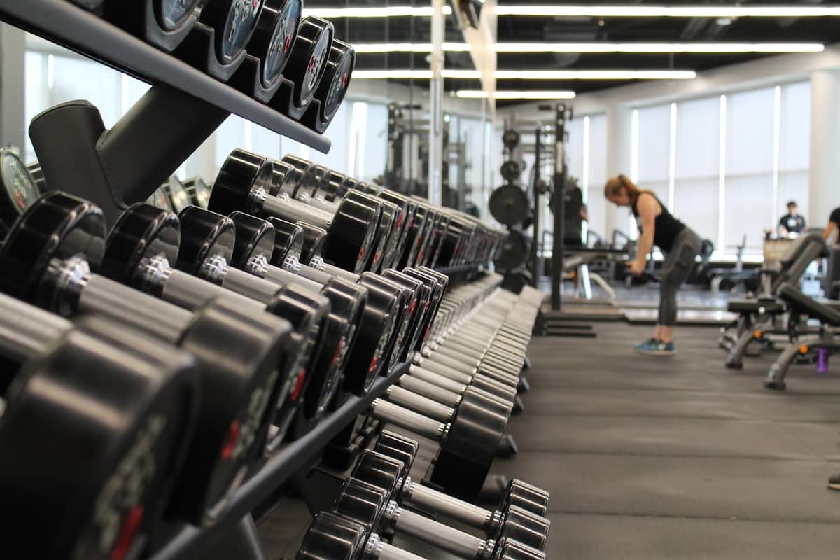 Rack of dumbbells along a gym floor, with a member training in the background